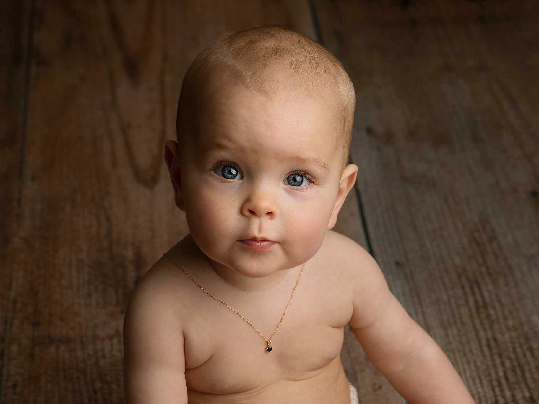 Liten flicka som är 6 månader sitter med ett fint halsband och tittar in i kameran när fotografen Anna Arvidsson fotograferar.