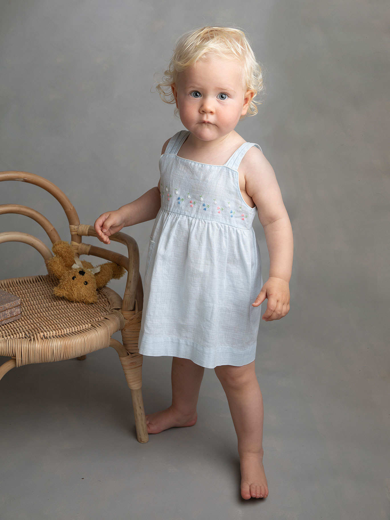 Flicka i blå klänning tittar fint rakt in i kameran under en fotografering i Malmö hos en barnfotograf.