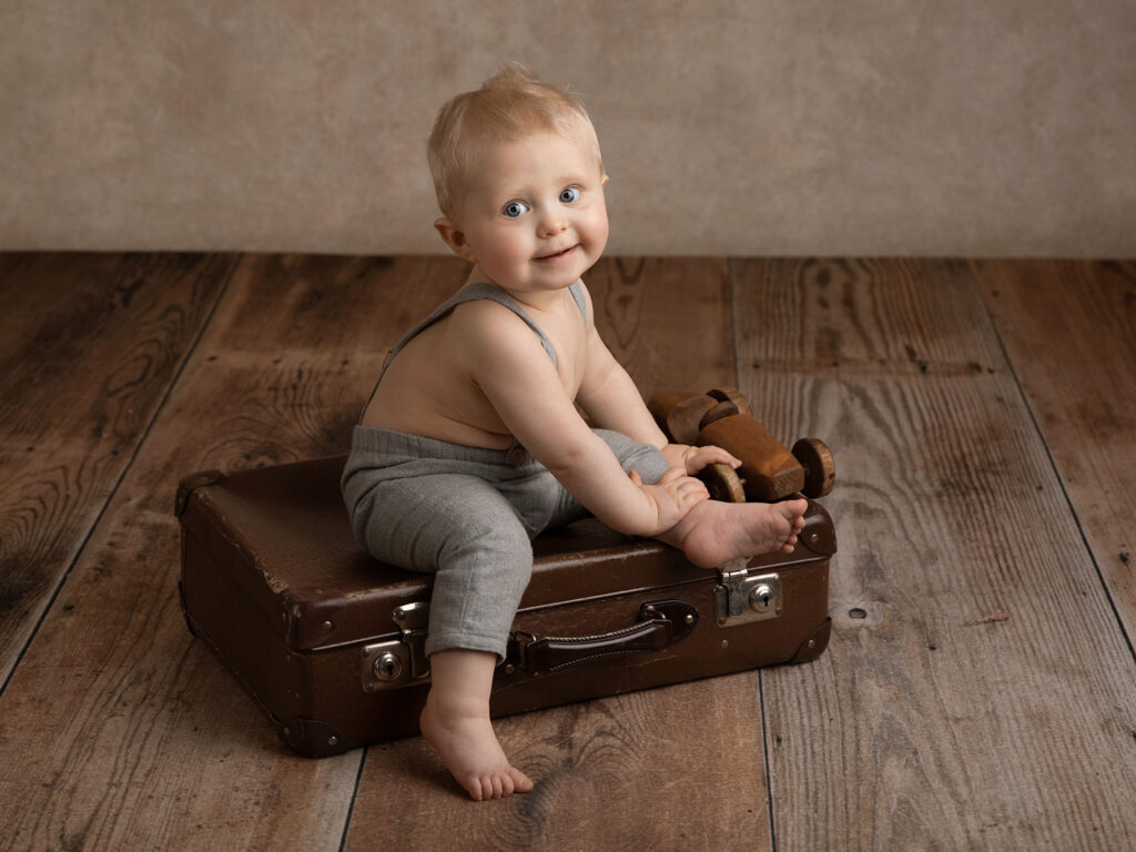 Pojke under en babyfotografering i studio i Malmö, sitter på en resväska och tittar fint in i kameran.
