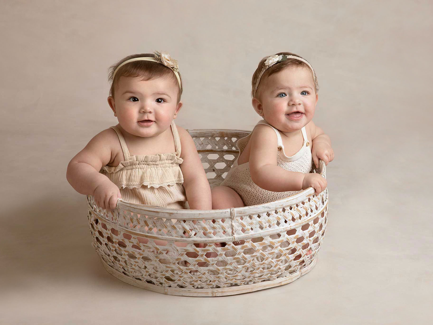 Två små tvillingflickor som är 8 månader blir fotograferade när de sitter i en korg under en fotografering i Malmö.