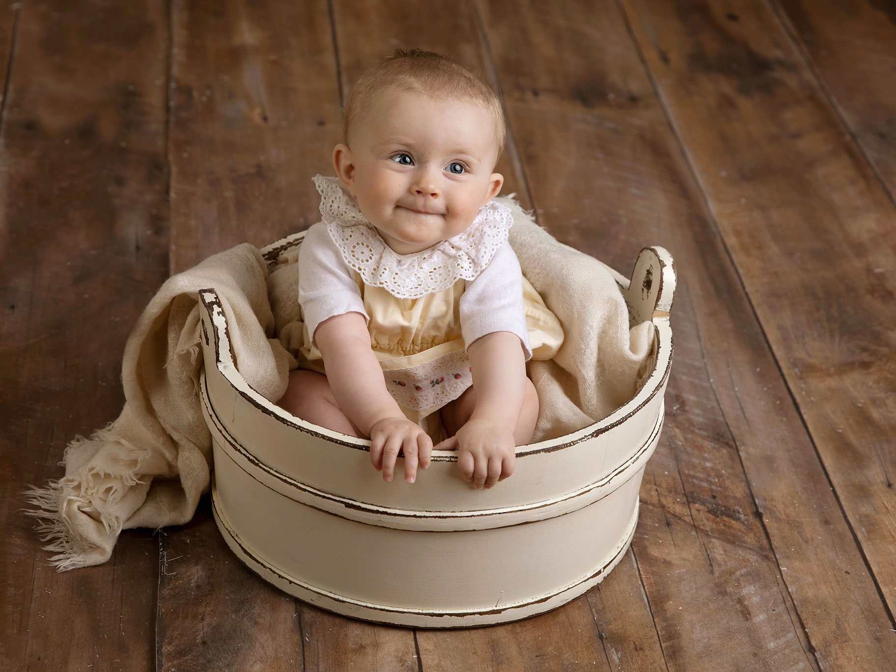 En söt liten baby tittar fint under en fotografering där hon sitter i en vit balja.