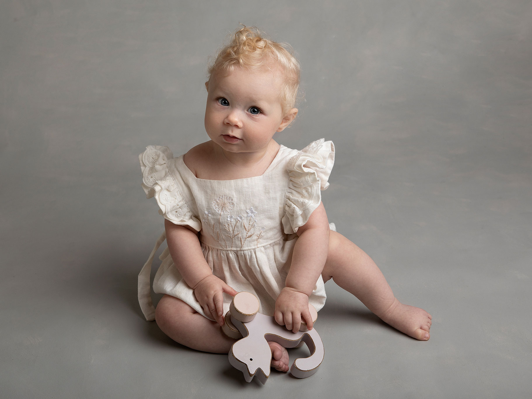 Flicka i vit klänning tittar rakt in i kameran under en fotografering i Malmö hos en barnfotograf.