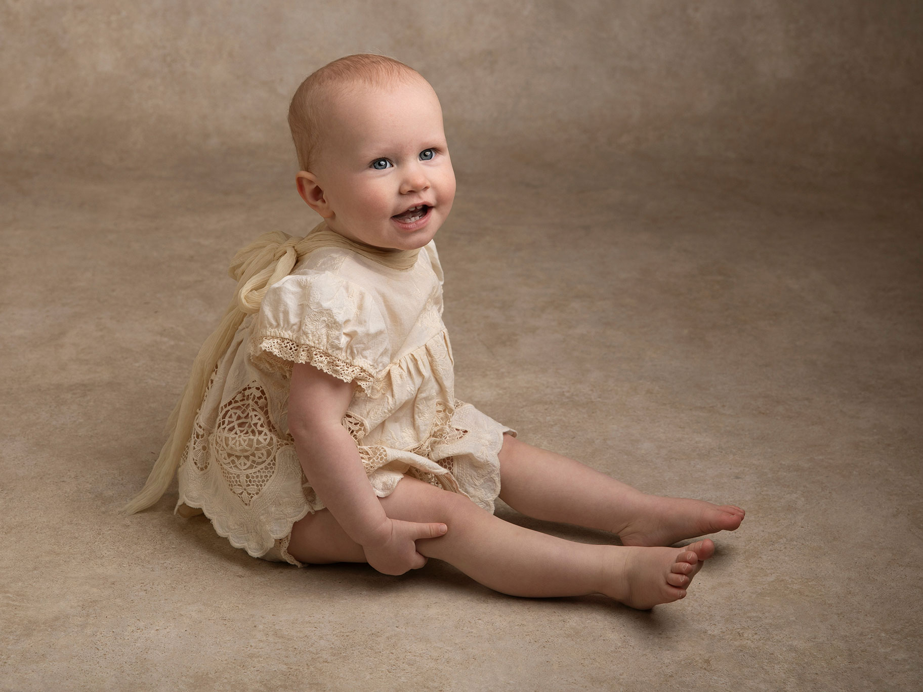 Liten flicka sitter på golvet i fina kläder och ler under en fotosession i Malmö.