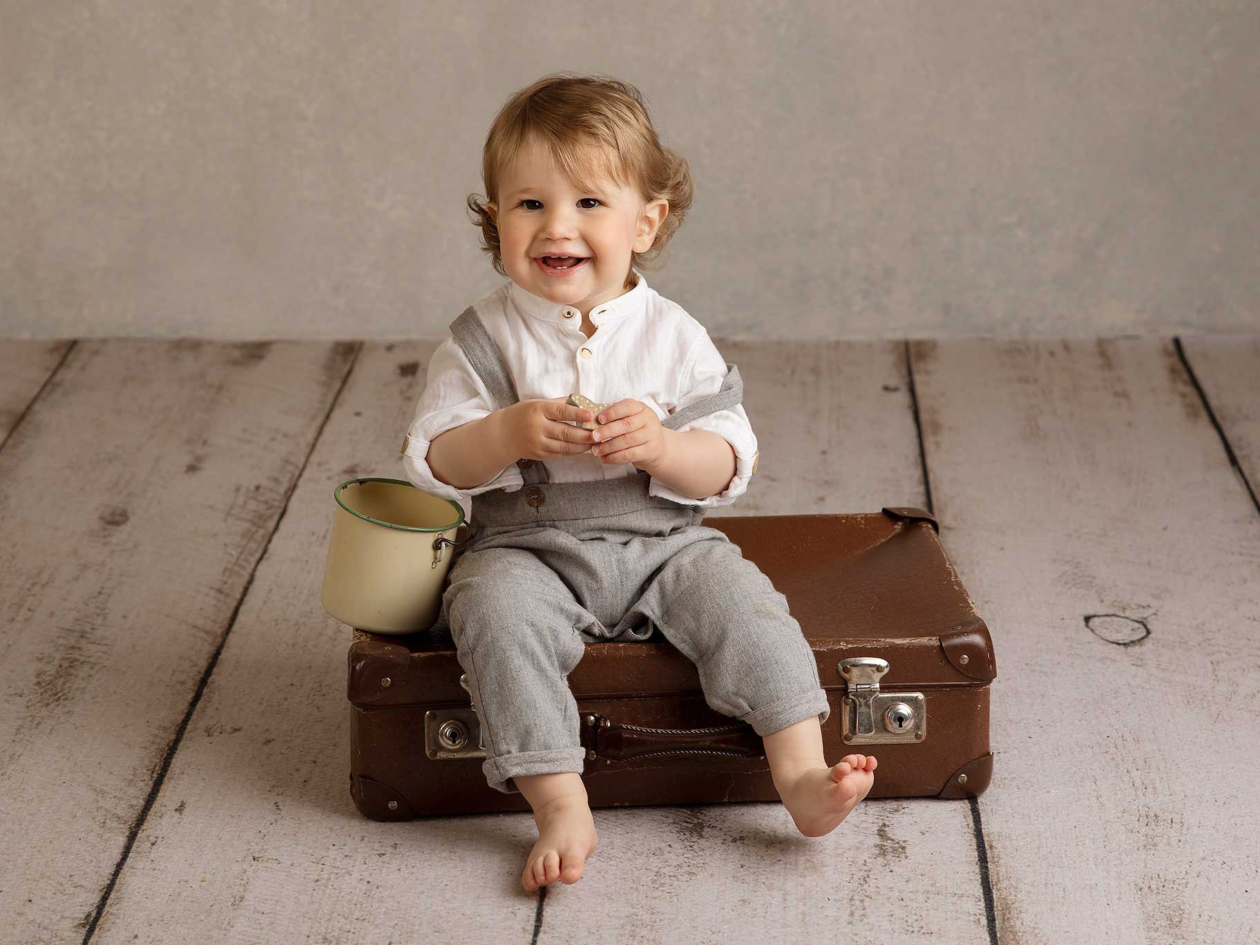 Liten pojke sitter på en resväska och skrattar i studion under fotografering.