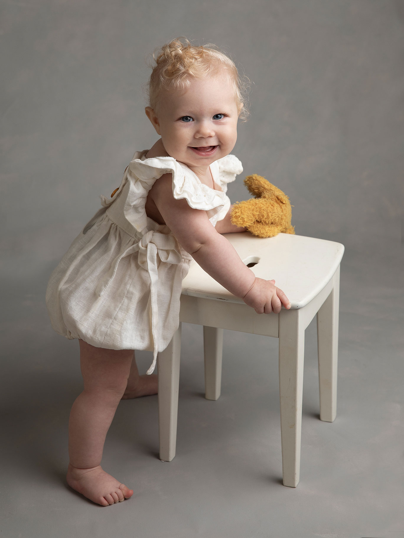 Flicka i vit klänning tittar fint rakt in i kameran under en fotografering i Malmö hos en barnfotograf.