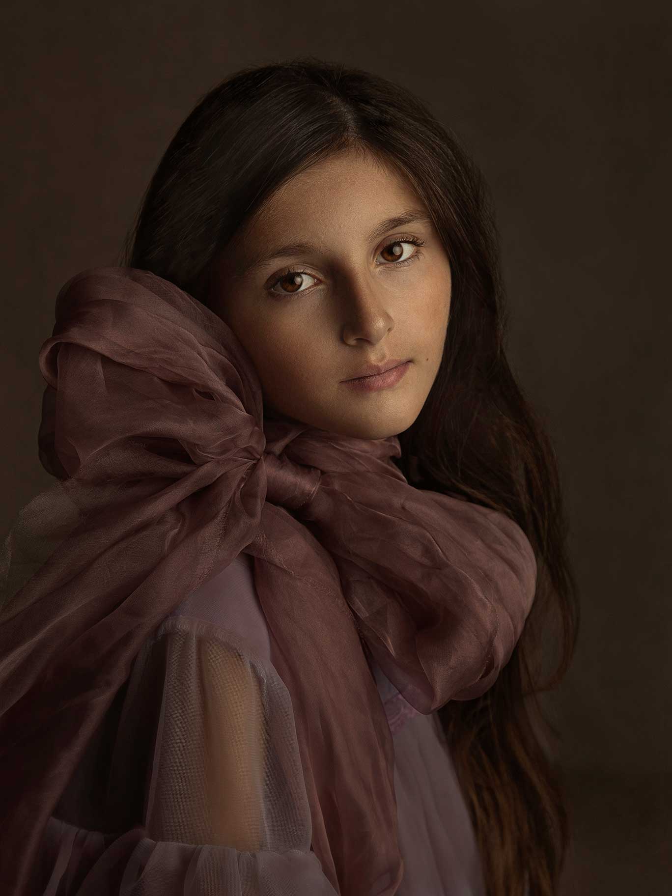 Porträtt av flicka med stor rosett i fin ljussättning där fotografen fångar barnets lugn och personlighet i konstnärlig studiomiljö.