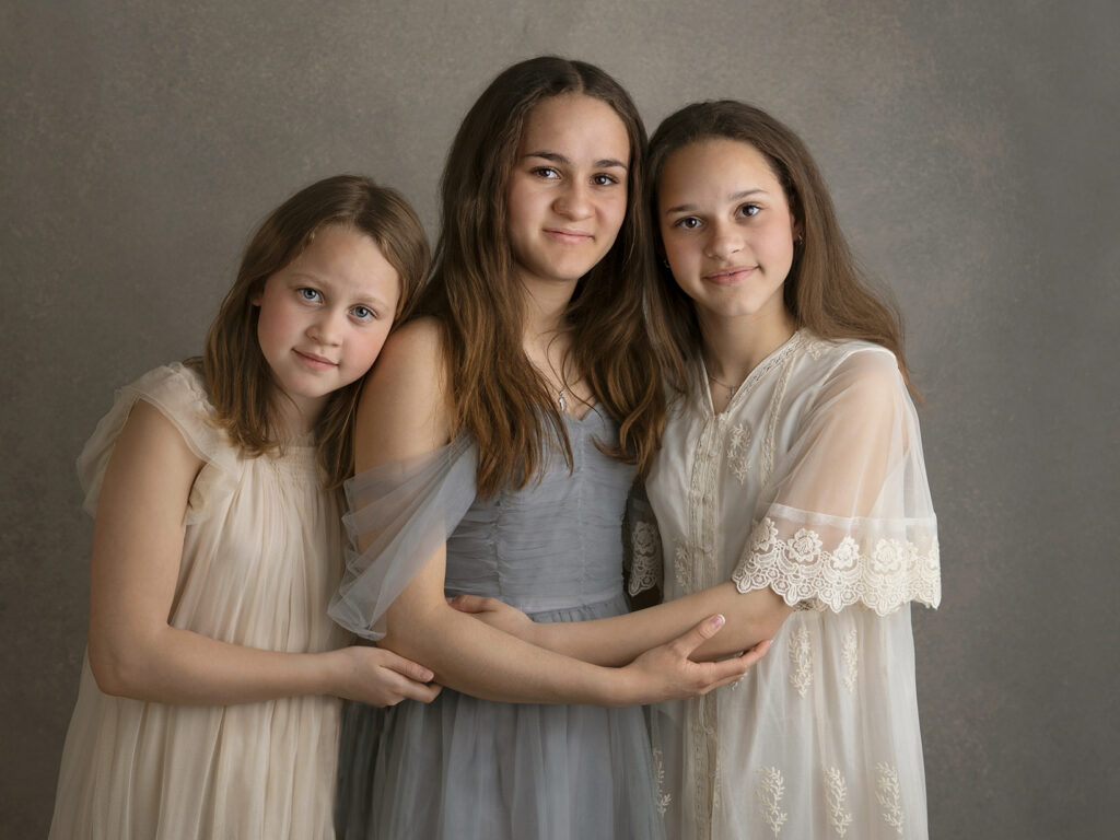 Tre flickor i vackra klänningar poserar framför kameran i studio i Malmö.