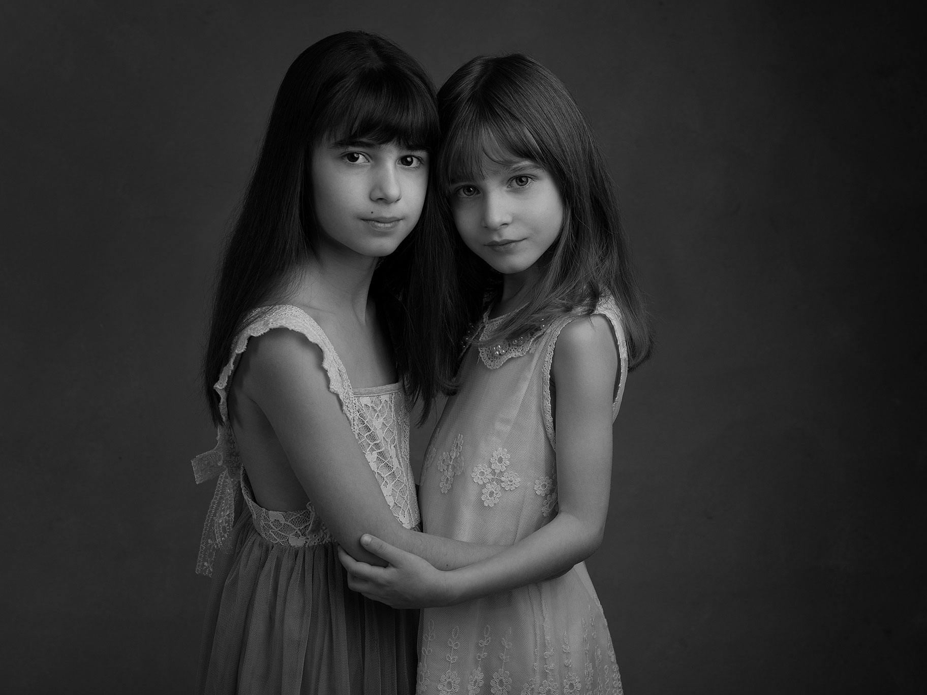 Två systrar håller om varandra i vintageinspirerad klädsel framför mörk bakgrund, fotograferat av Anna Arvidsson.