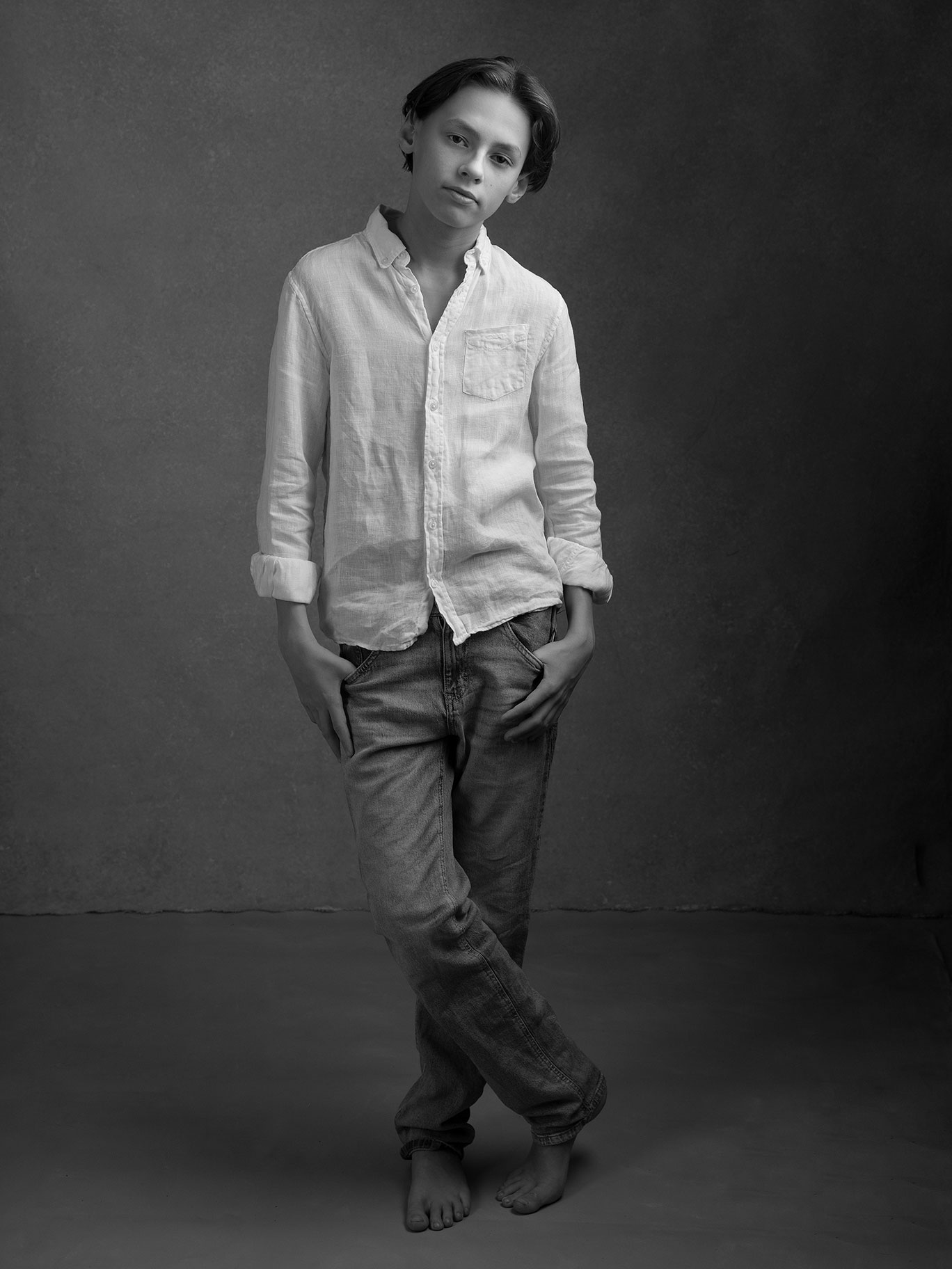 Cool och avslappnad bild i svartvitt av en pojke i vit skjorta och jeans, fotograferat i en studio i Malmö.