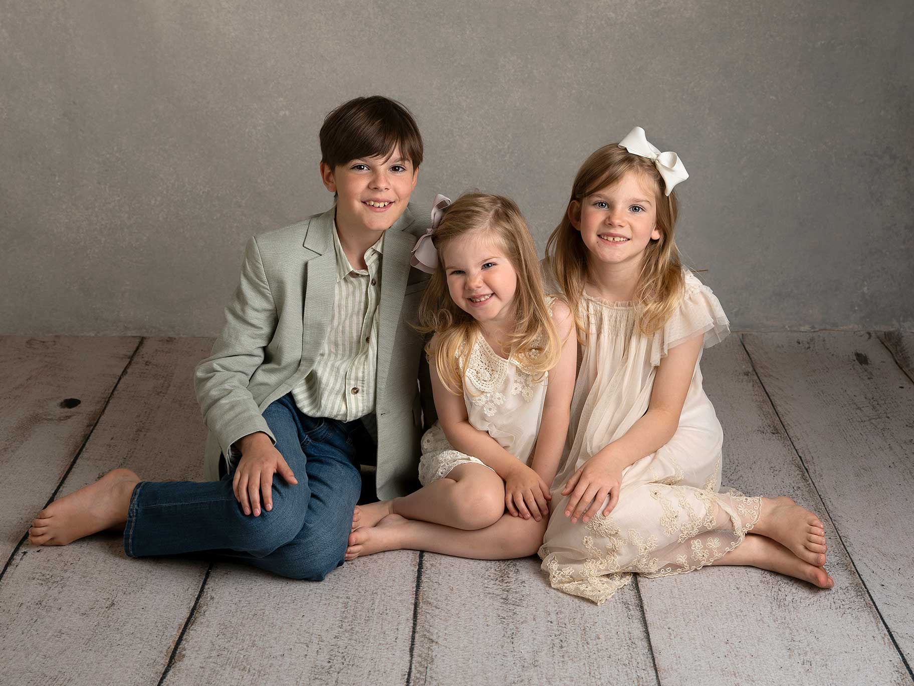 Tre syskon sitter tillsammans på studiogolvet och blir fotograferade av en familjefotograf i Malmö, Skåne.