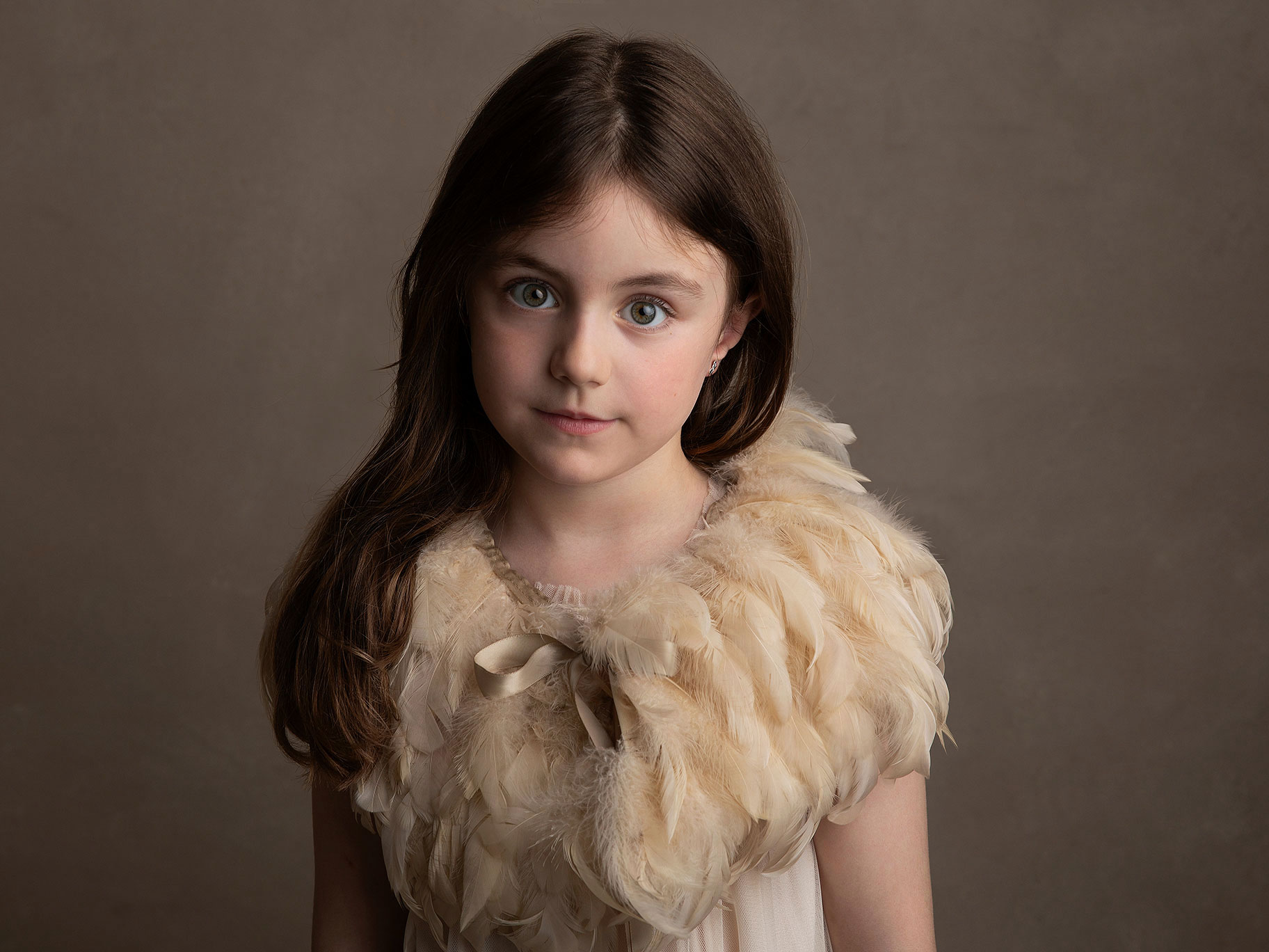 Flicka med fjäderkrage tittar fint in i kameran i studio i Malmö.