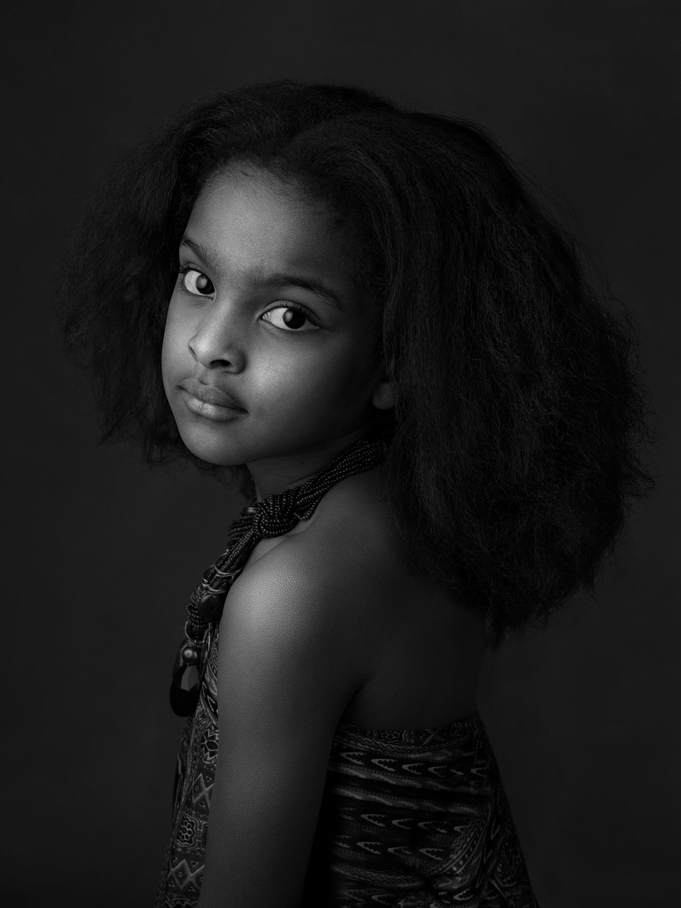Barnporträtt i svartvitt av liten flicka som tittar så fint in i kameran i studio i Malmö.
