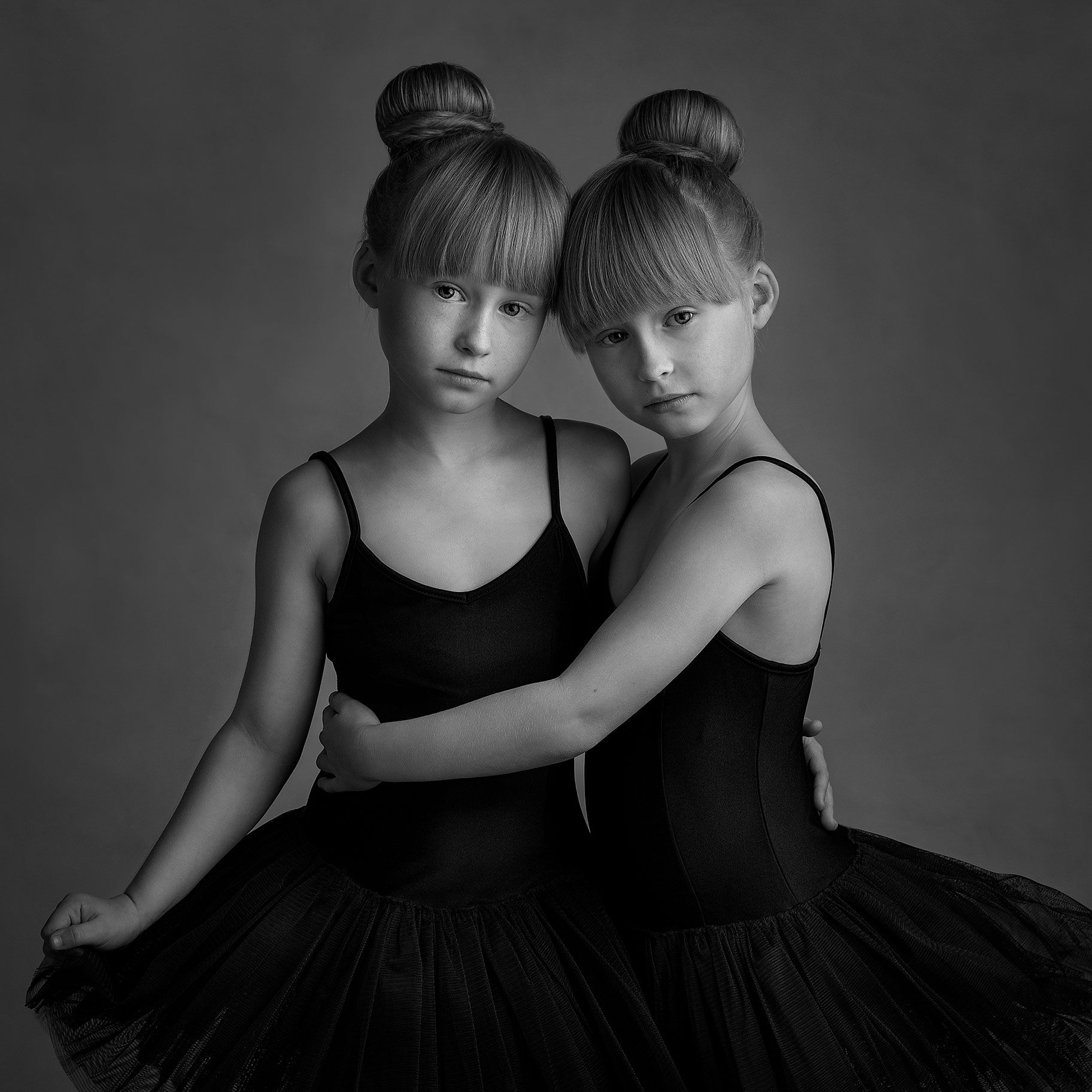 Studioporträtt i på två tvillingar som har balettklänningar på sig.
