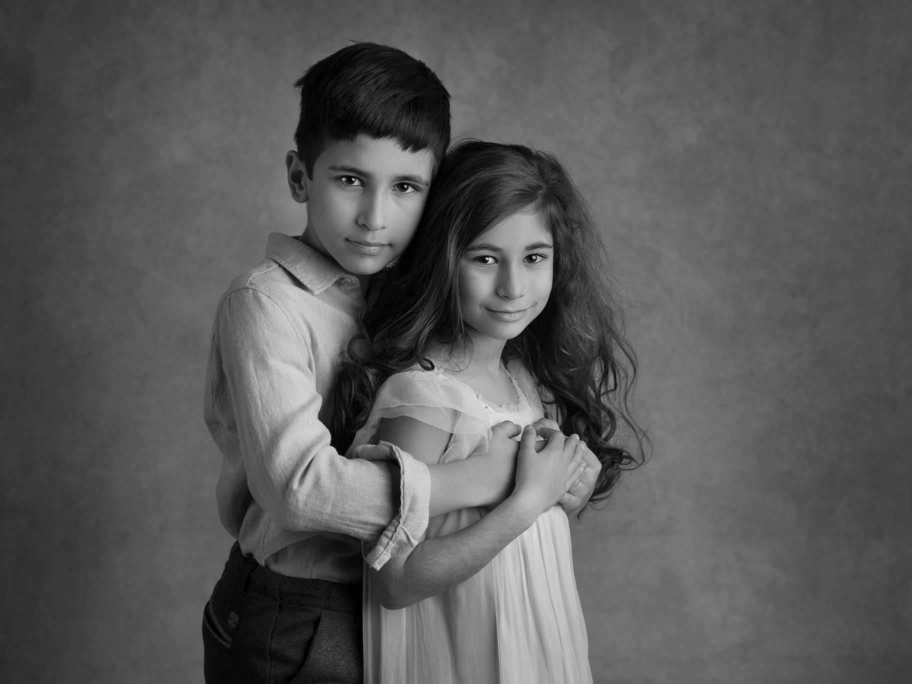Två syskon håller om varandra och tittar fint in i kameran.