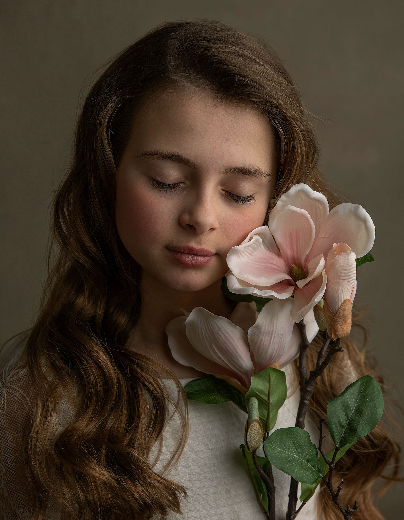 Känslofyllt porträtt av barn som blundar och håller en blomma i studiomiljö med varm ljussättning.