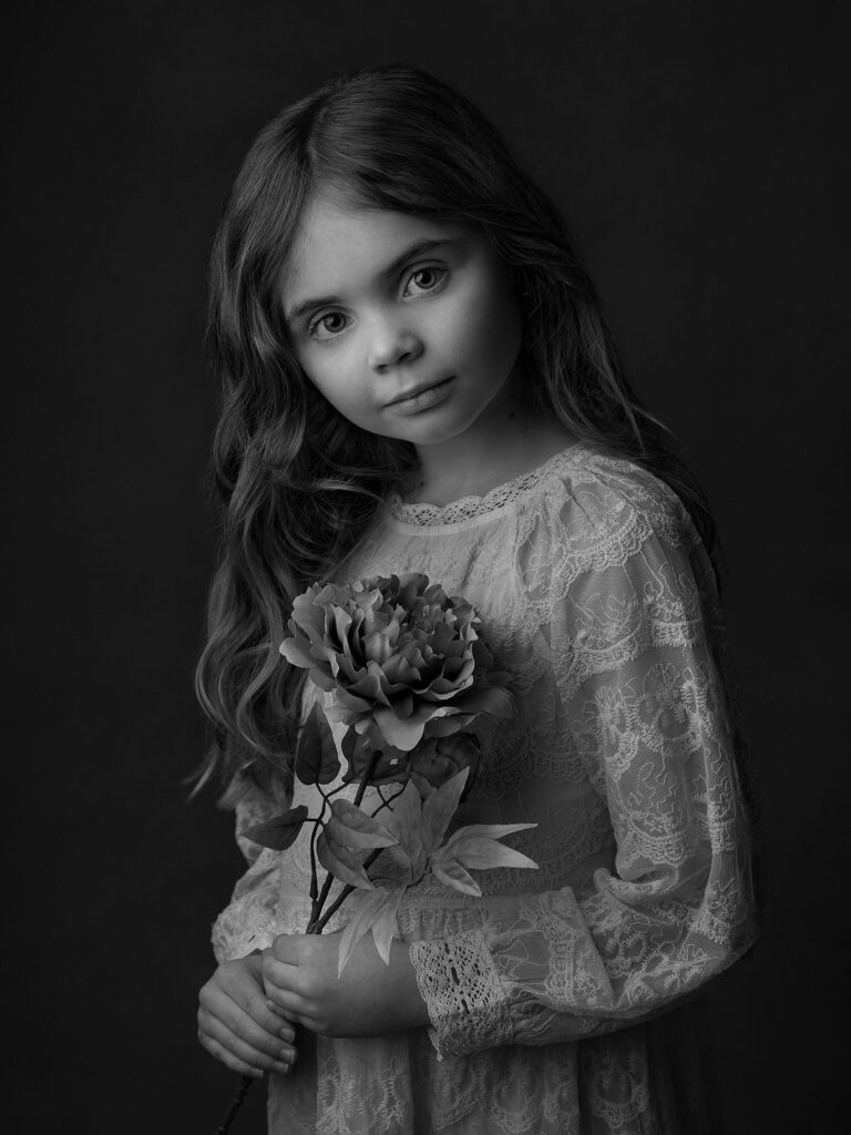 Flicka håller en blomma och bär en vit spetsklänning under en fotografering i Malmö.