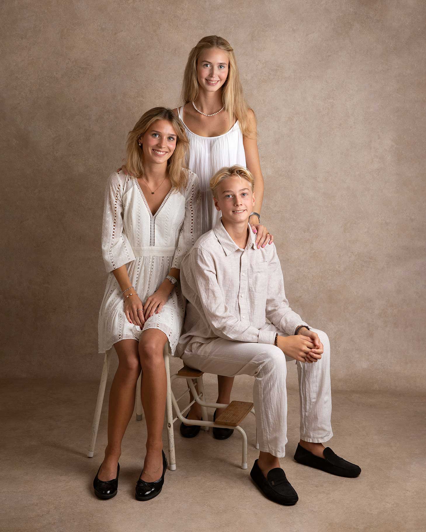 Tre syskon som är tonåringar sitter och blir fotograferade i en studio i Malmö med vita fina kläder.