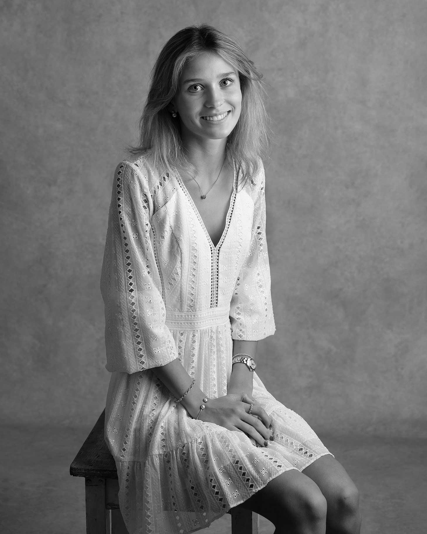 Ung tjej i vit klänning sitter och ler mot fotografen under en fotografering i Malmö.