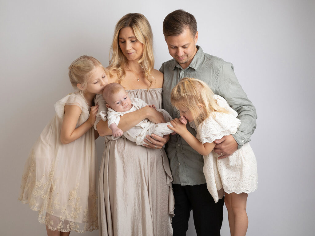 Familj klädd i ljusa pastellfärger poserar framför grå bakgrund i Anna Arvidssons fotostudio.