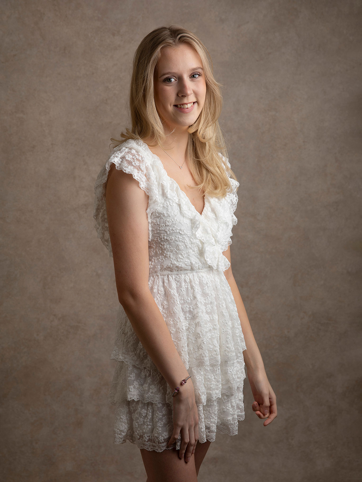 Ung tjej i vit klänning står och ler mot fotografen under en fotografering i Malmö.