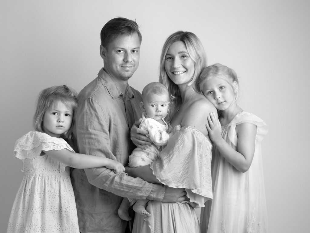 Svartvitt fotografi av en familj med tre barn, alla tittar fint in i kameran under en fotografering i Malmö.