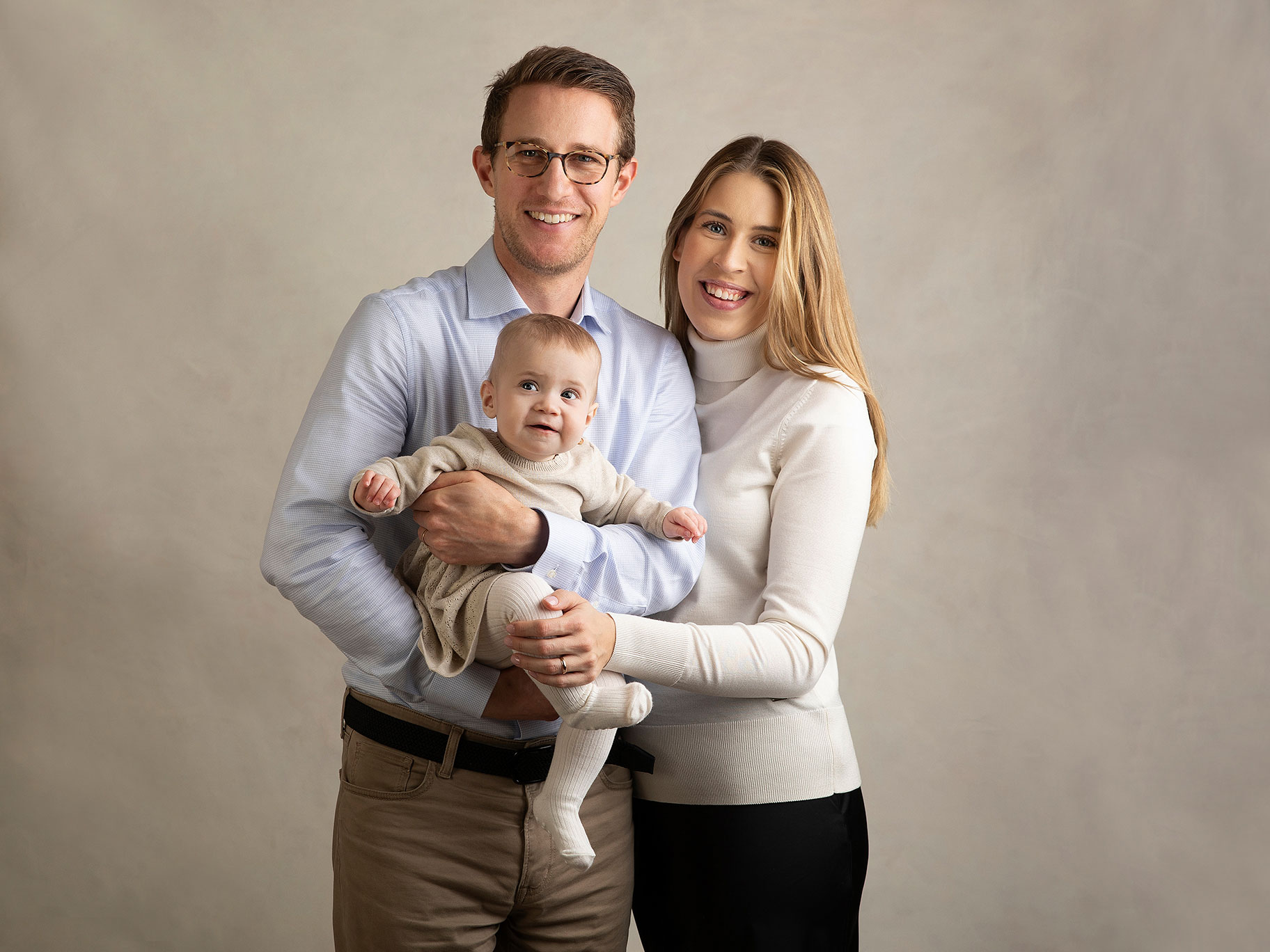 Familj med ett litet barn står tätt tillsammans framför grå bakgrund i studion.