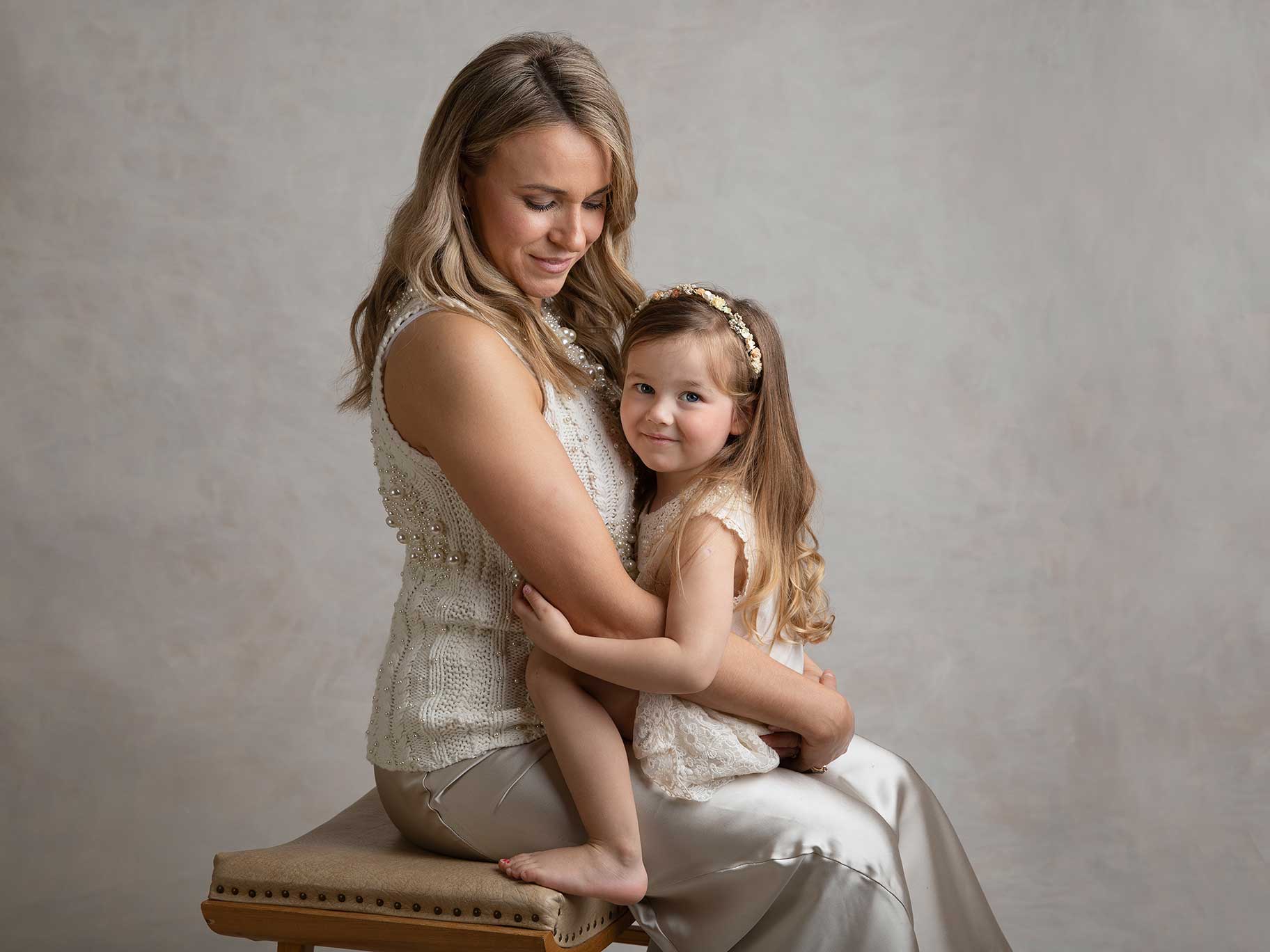 Vacker mamma med sin lilla dotter i famnen, de bär båda vackra klänningar.