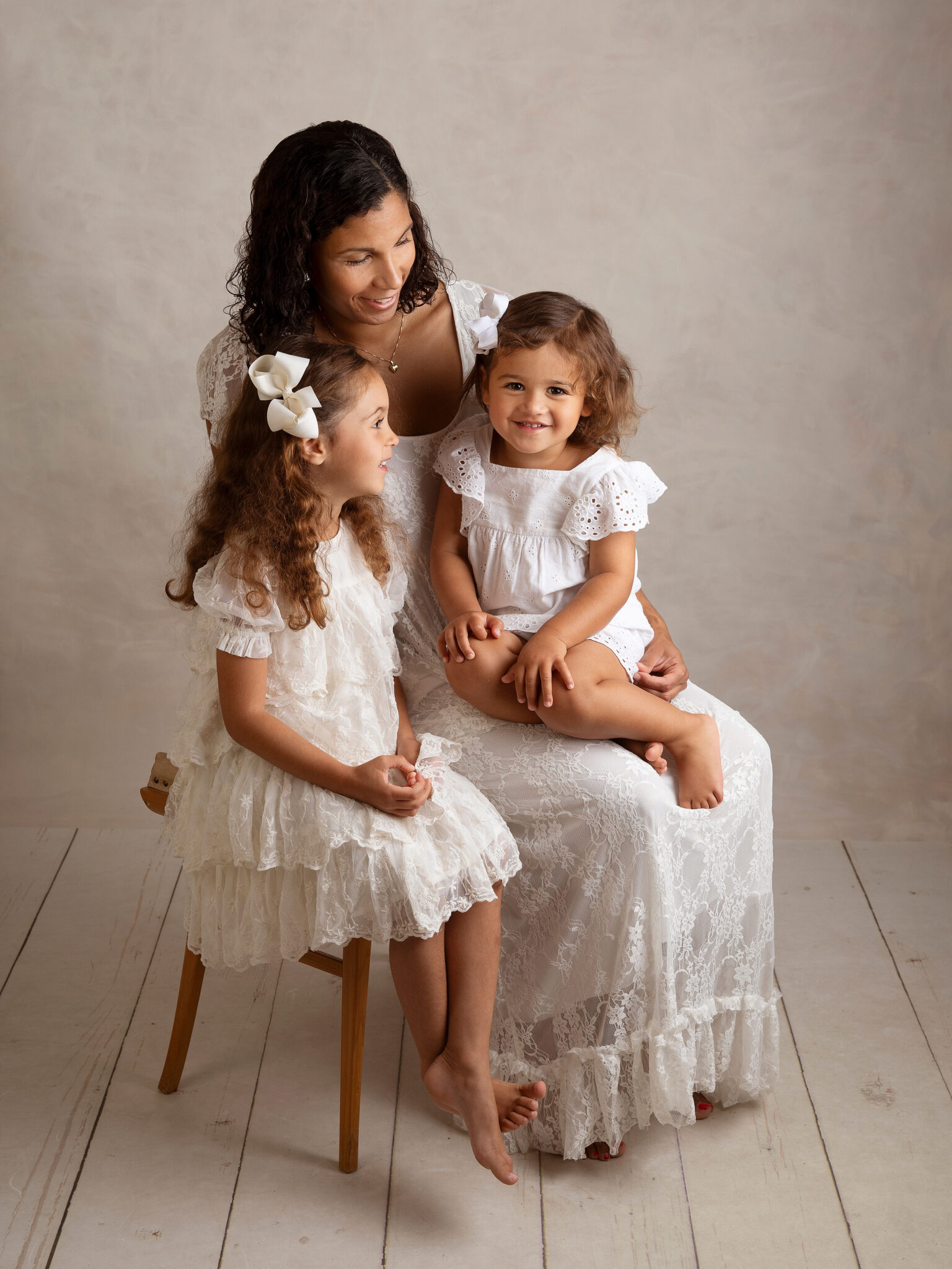 Mamma och två döttrar i fina, vita klänningar tittar på varandra i studion i Malmö.