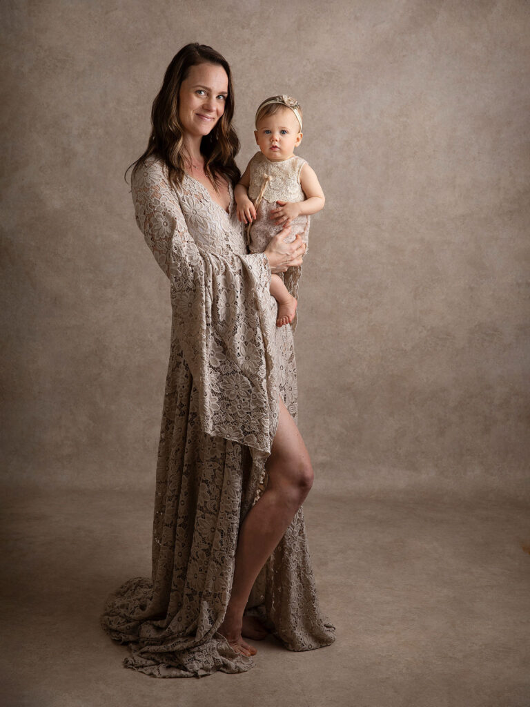 Mamma i fin spetsklänning tittar stolt mot kameran med sin flicka i famnen.