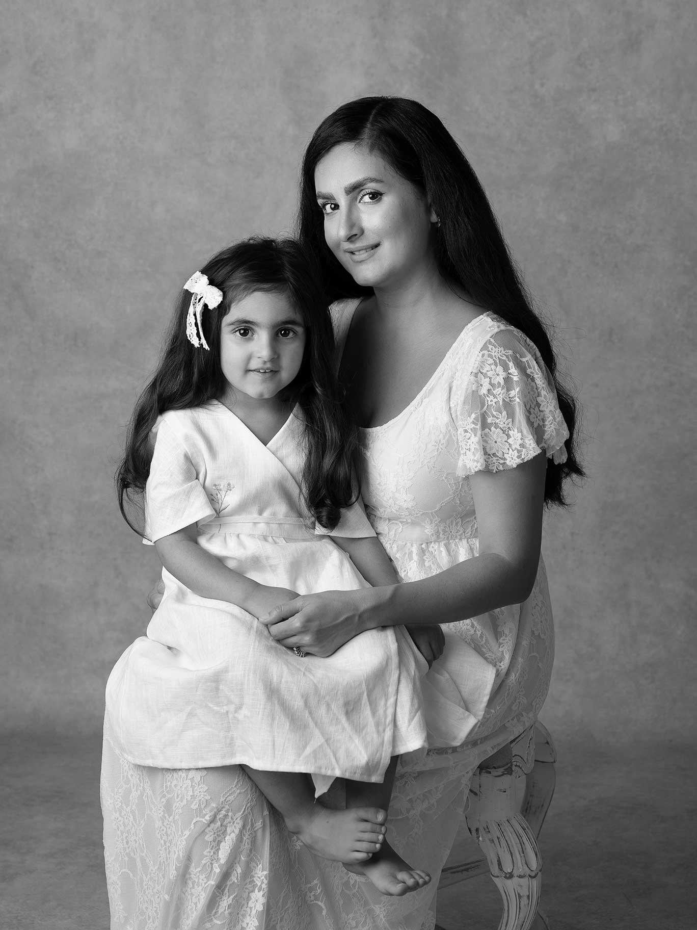 Svartvitt fotografi av en mamma som har en flicka i knäet, båda ler och tittar in i kameran under en fotografering i Malmö.