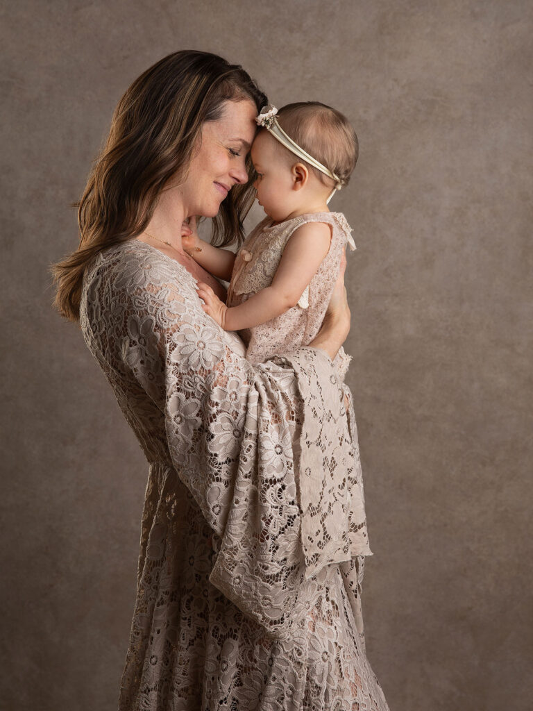 Mamma i vacker klänning håller pannan tätt intill sin lilla baby under en fotografering i Malmö.