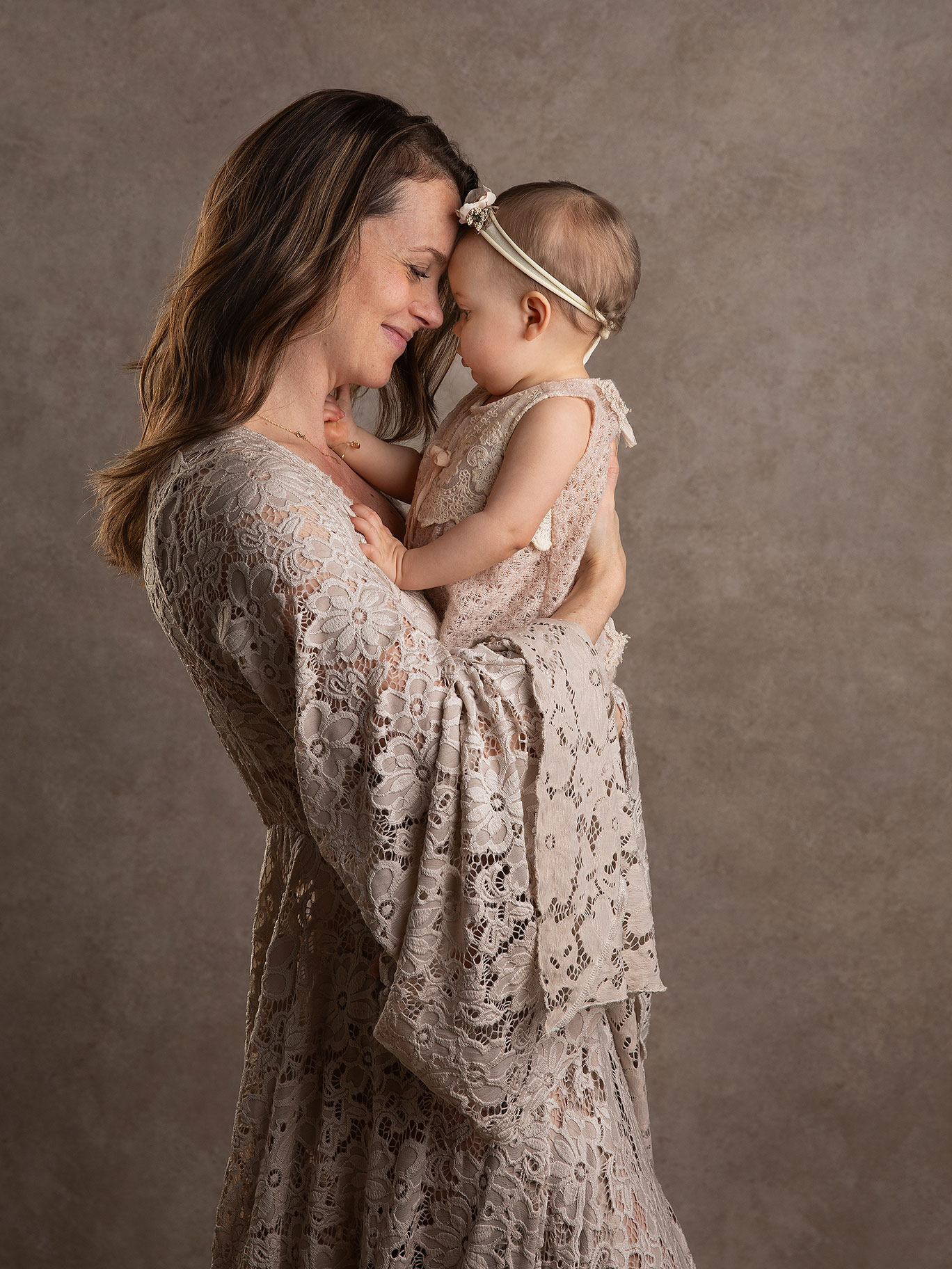 Mamma i vacker klänning håller pannan tätt intill sin lilla baby under en fotografering i Malmö.