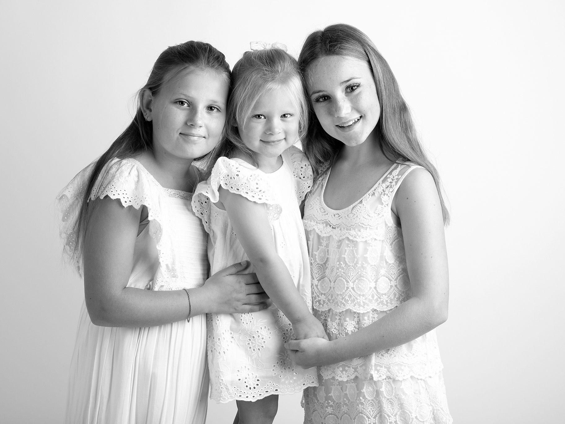 Tre systrar i fina, vita klänningar ler mot kameran, i studion i Malmö