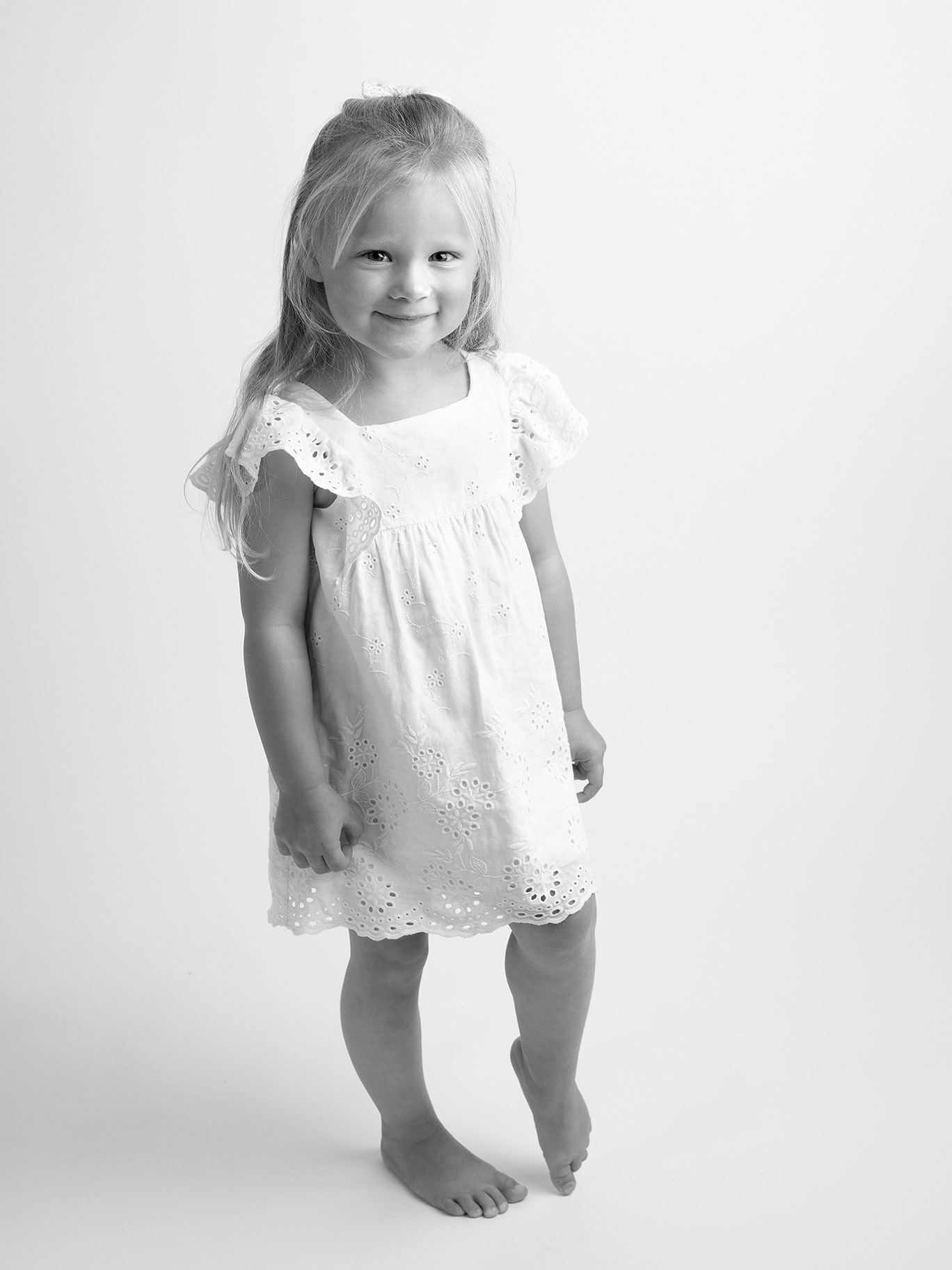 Svartvit bild med flicka i vit klänning där fotografen fångat ett härligt leende.