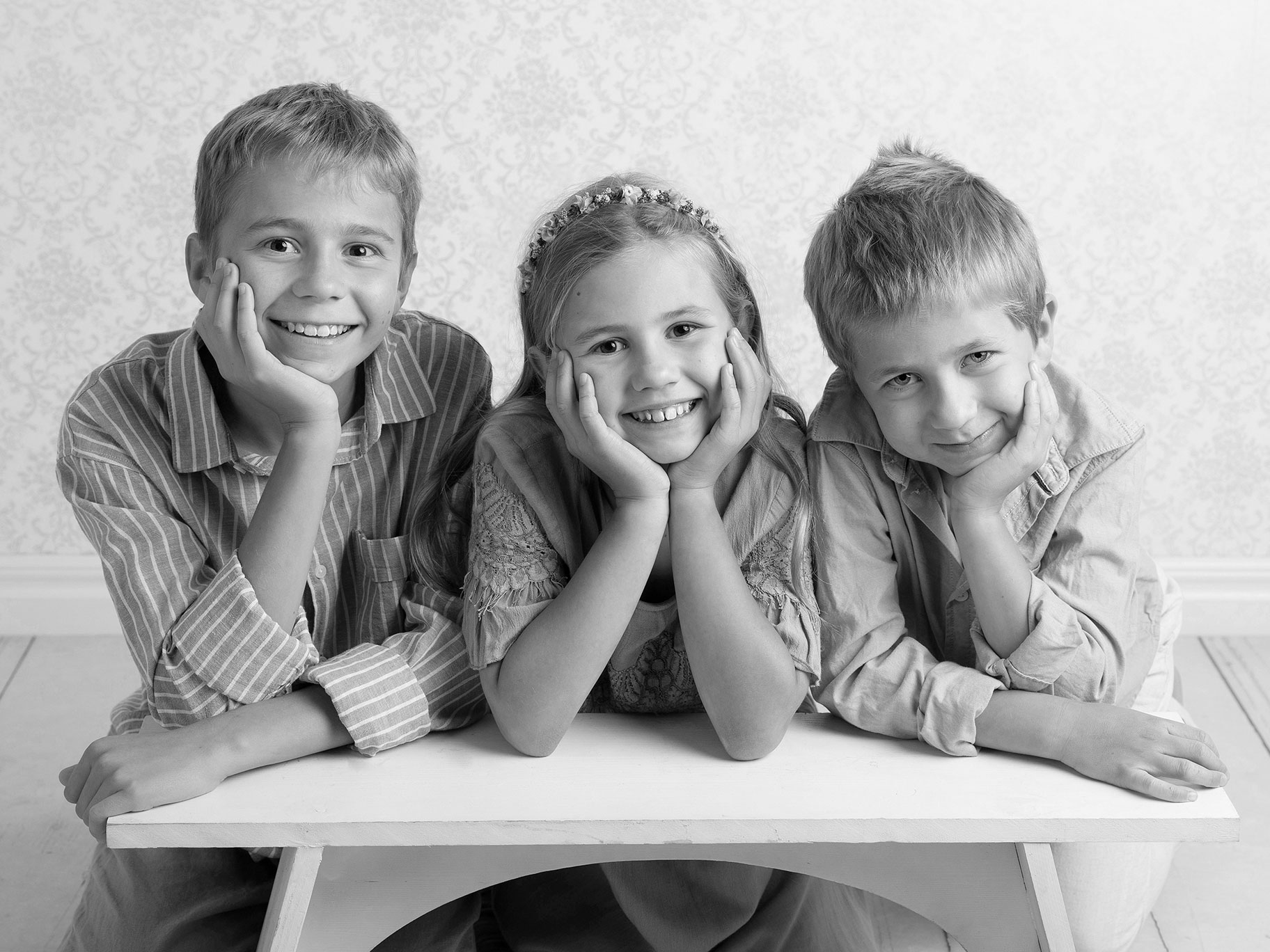 Tre syskon tittar fint mot kameran under en fotografering i studio i Malmö.
