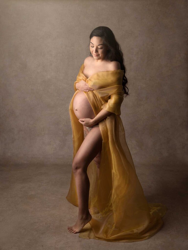 Gravid kvinna med händerna på magen, omgiven av mjukt ljus i studion i Malmö.