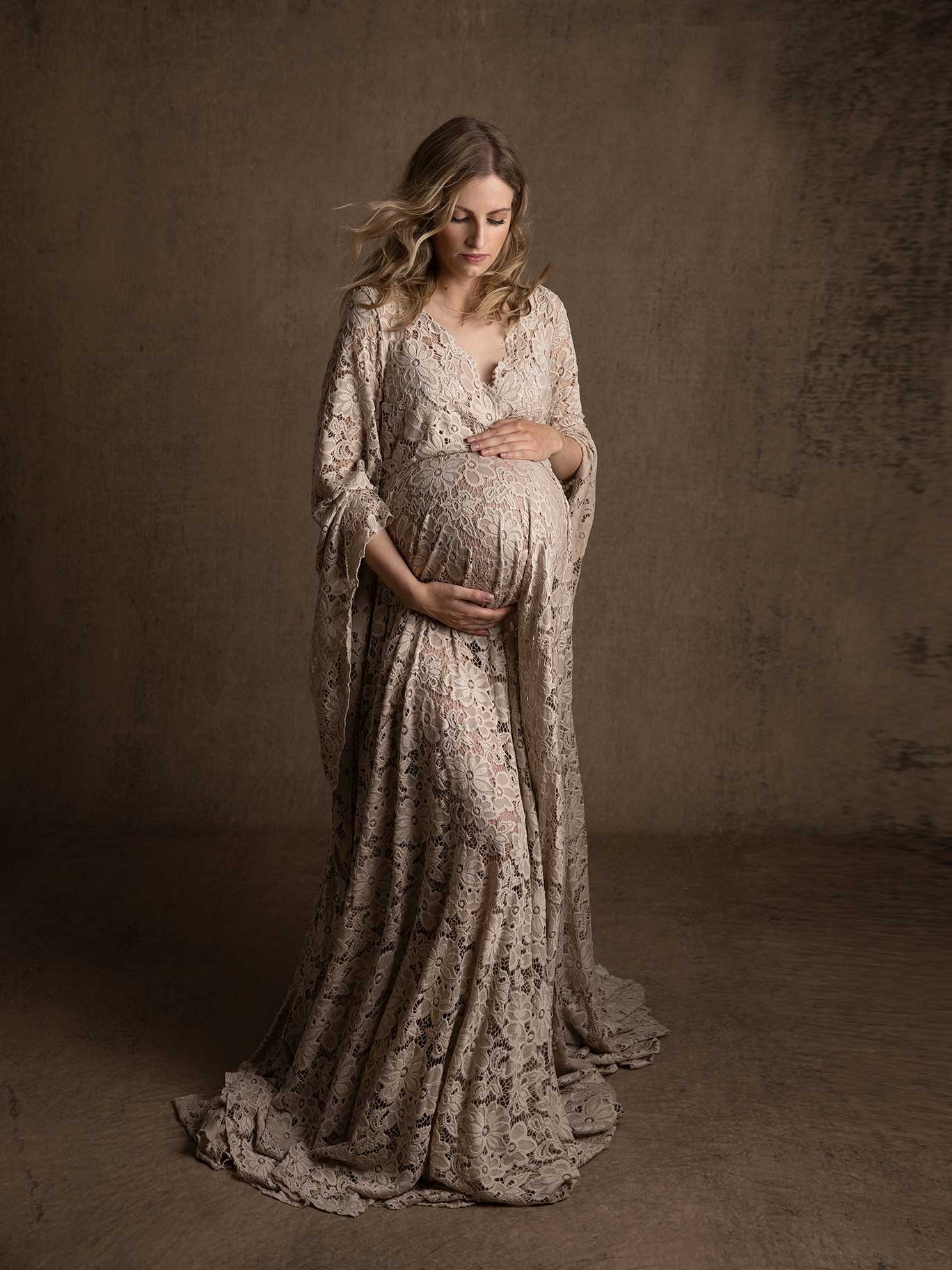 Gravid kvinna håller händerna på magen och tittar ner under lugn och harmonisk fotografering i studio.