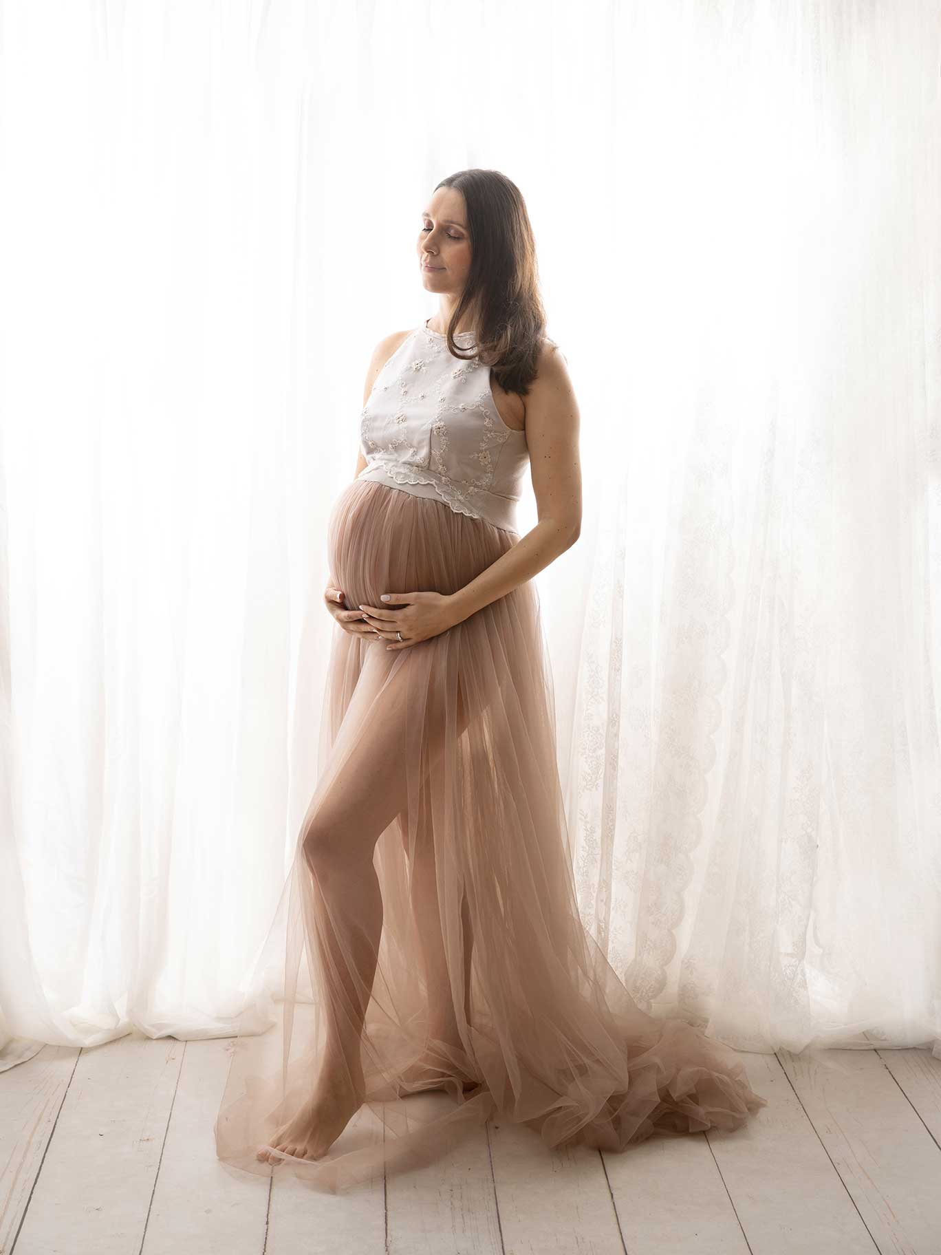 Gravid kvinna i vacker klänning poserar framför ljus bakgrund i Fotostudio Anna Arvidsson.