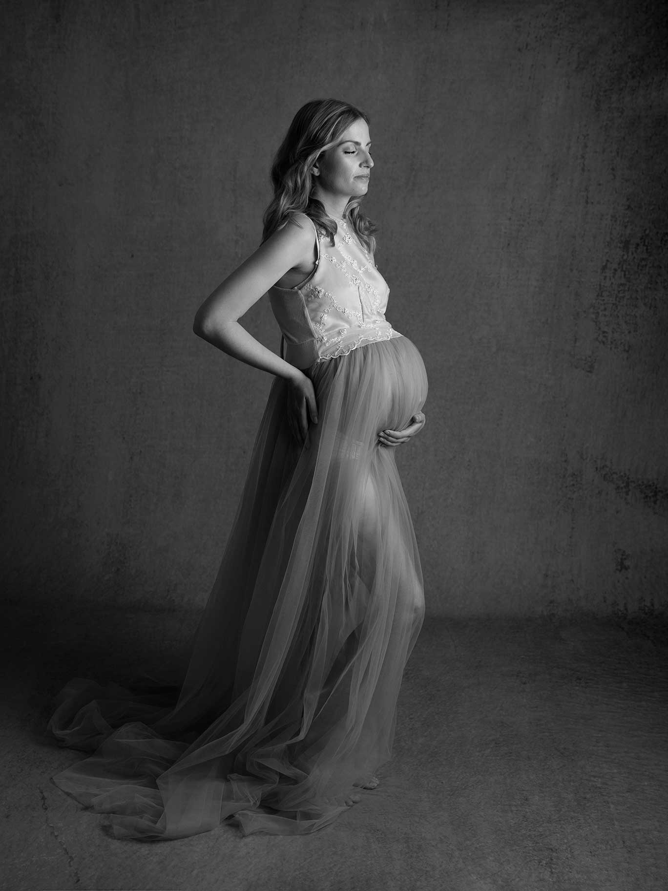 Stilrent gravidporträtt i klassisk pose mot mörk bakgrund, taget i studio i Malmö.