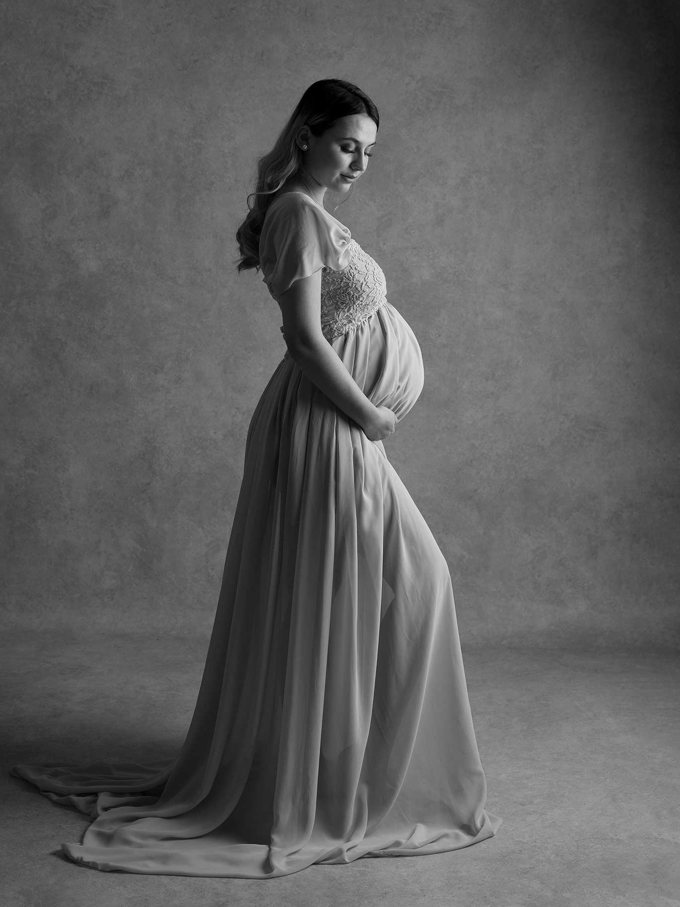 Vacker svartvit bild av gravid tjej som har på sig en vacker klänning med långt tyg.