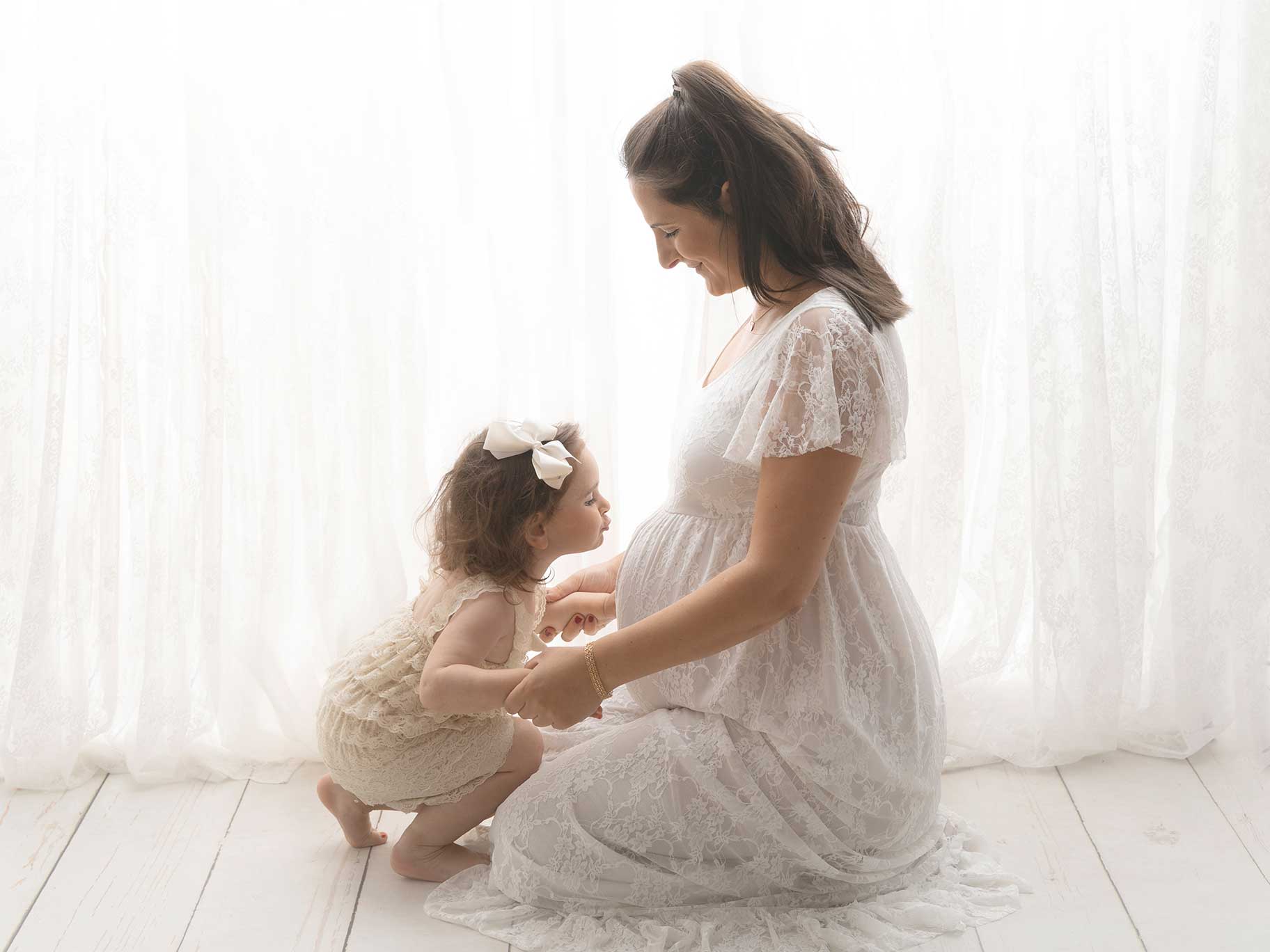 Gravid mamma med sin lilla dotter som ska bli storasyster, där flickan pussar magen i studion i Malmö.