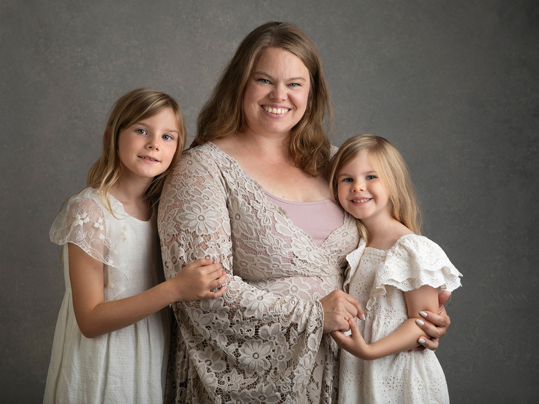 En mamma och två flickor ler stort mot kameran. De har vackra klänningar på sig och ser ut att trivas i fotostudion i Malmö.