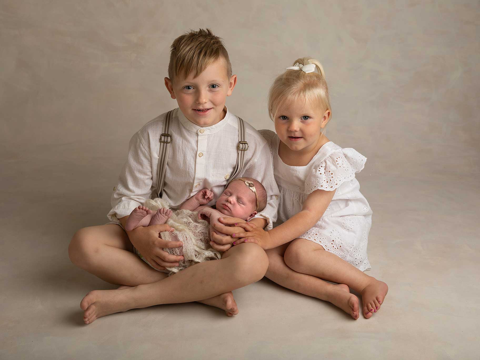 Nyfödd flicka i famnen på storasyskon fotograferad när hon sover hos en barnfotograf i Malmö.