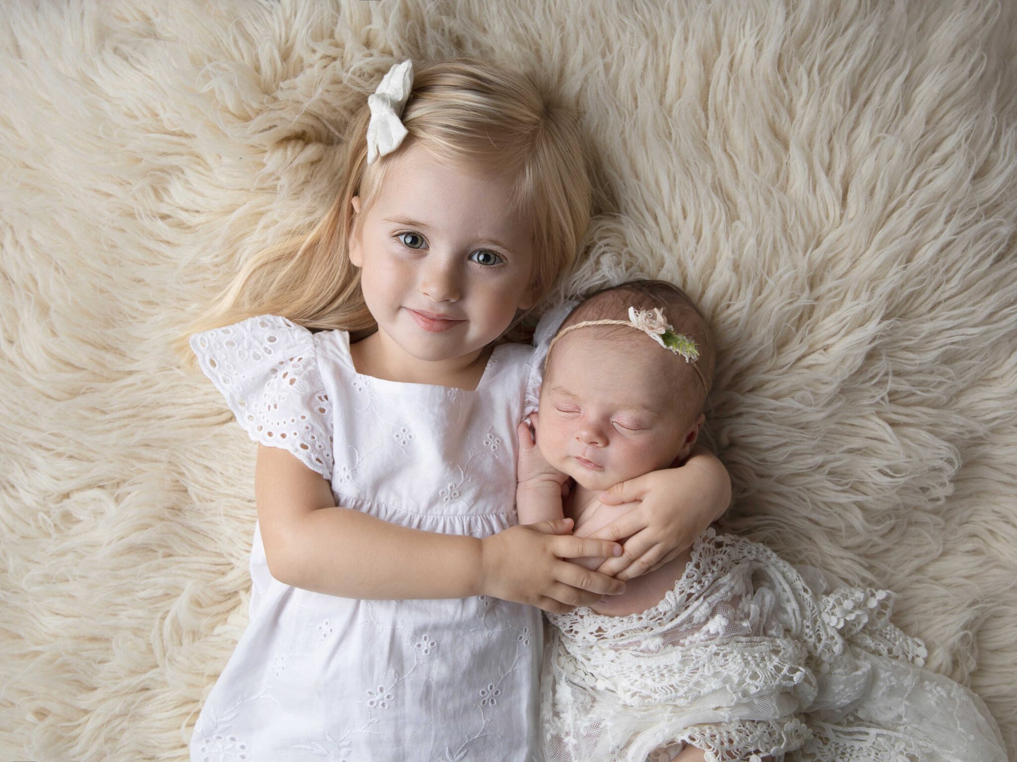 Stolt storasyster med liten nyfödd, bild tagen under en nyföddfotografering i en studio i Malmö.