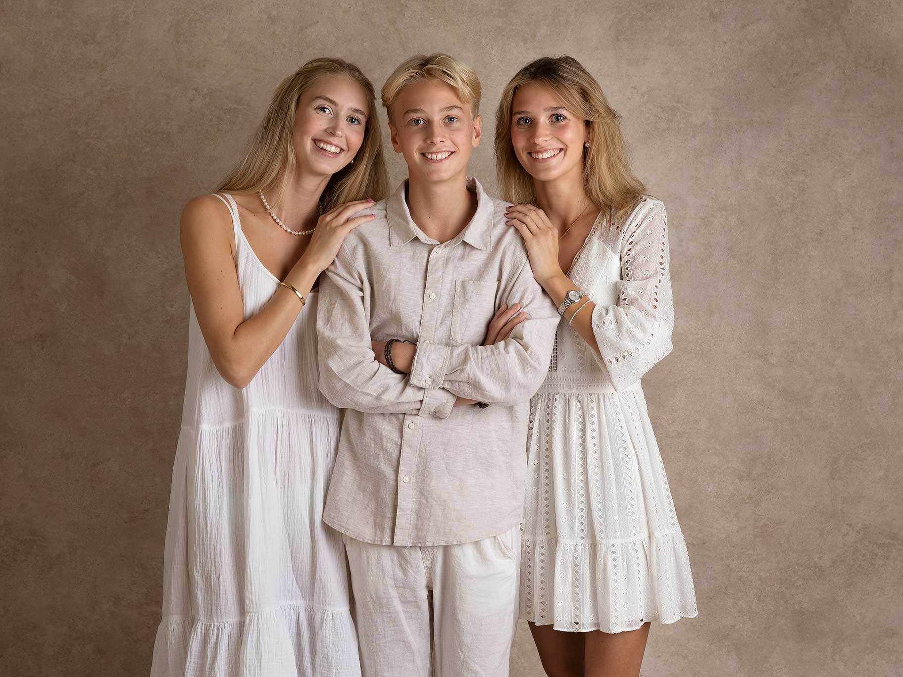 Två systrar och en bror i vita fina kläder står tillsammans under en fotografering i Malmö.