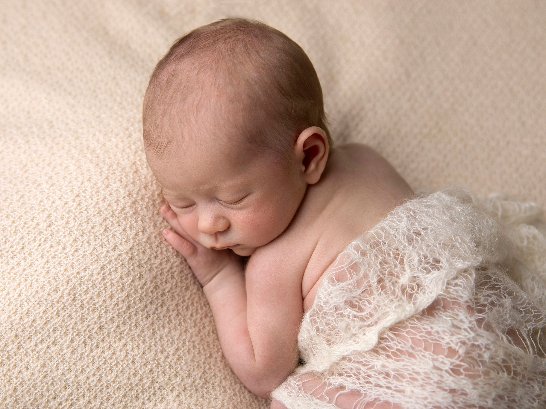 Liten nyfödd baby sover med en vit filt runt sig.