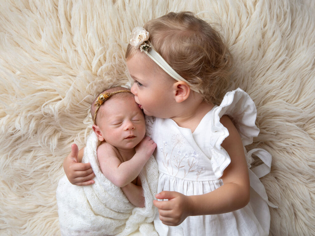 En nybliven storasyster pussar sin lillasyster på pannan under en fotografering med Anna Arvidsson i Malmö.
