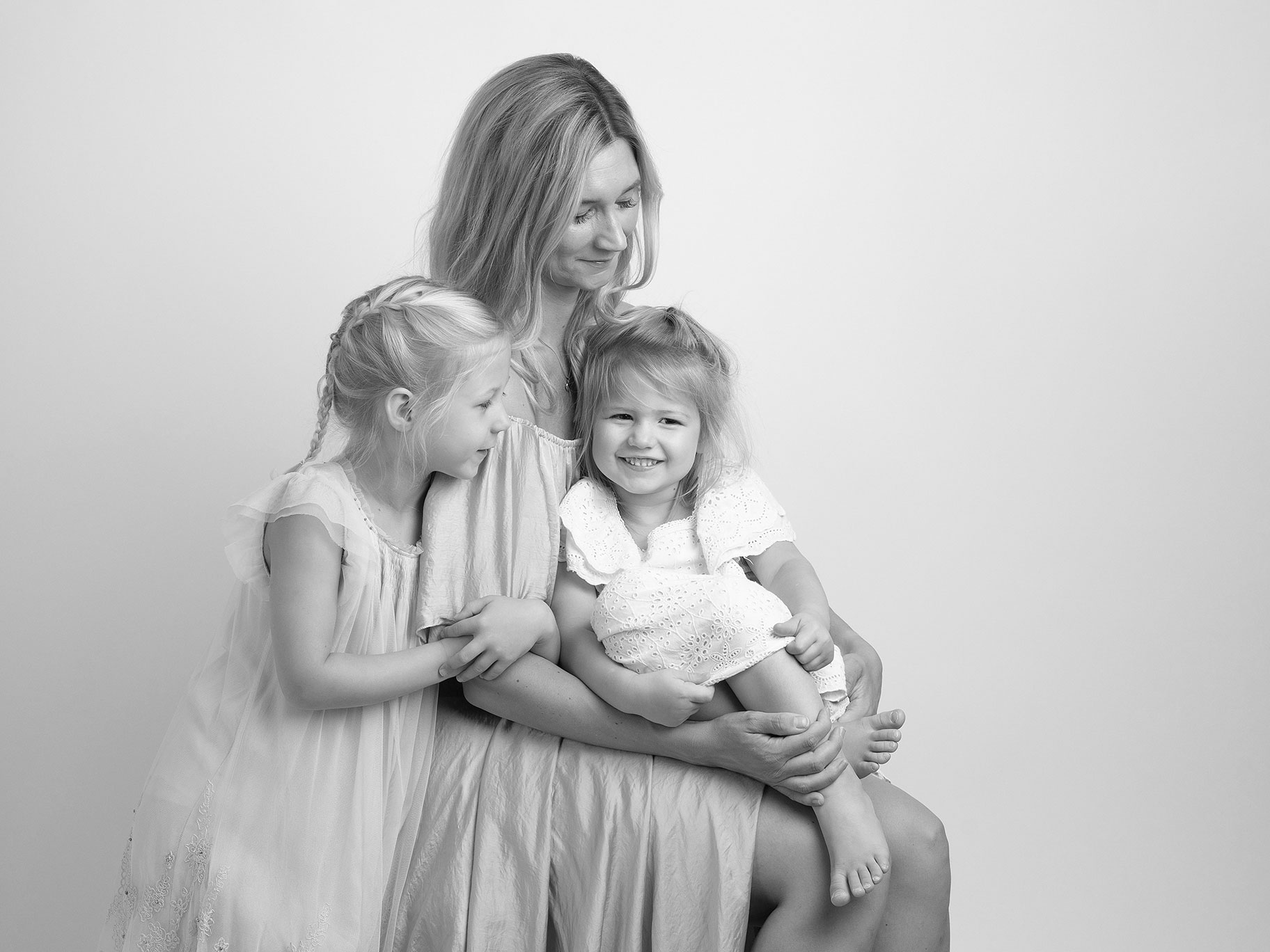 Mamma håller sina barn i famnen och de ler och ser ut att trivas framför kameran under en familjefotografering i Malmö.