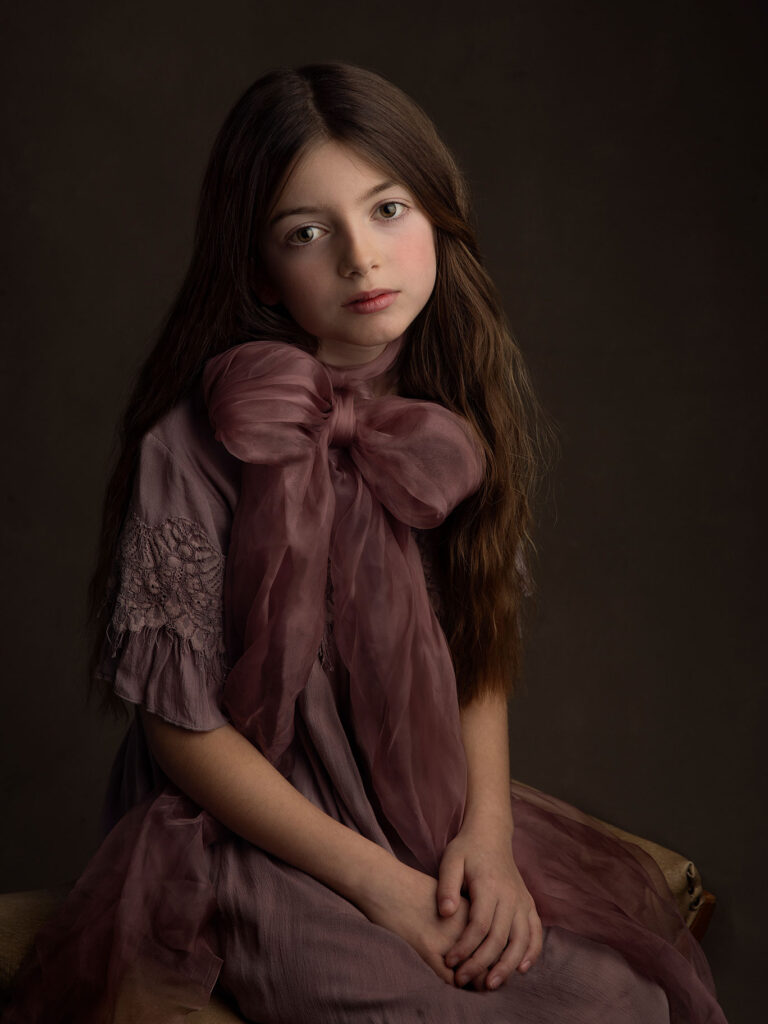 Vacker och konstnärlig bild av en flicka med brunt långt hår med stor lila rosett.