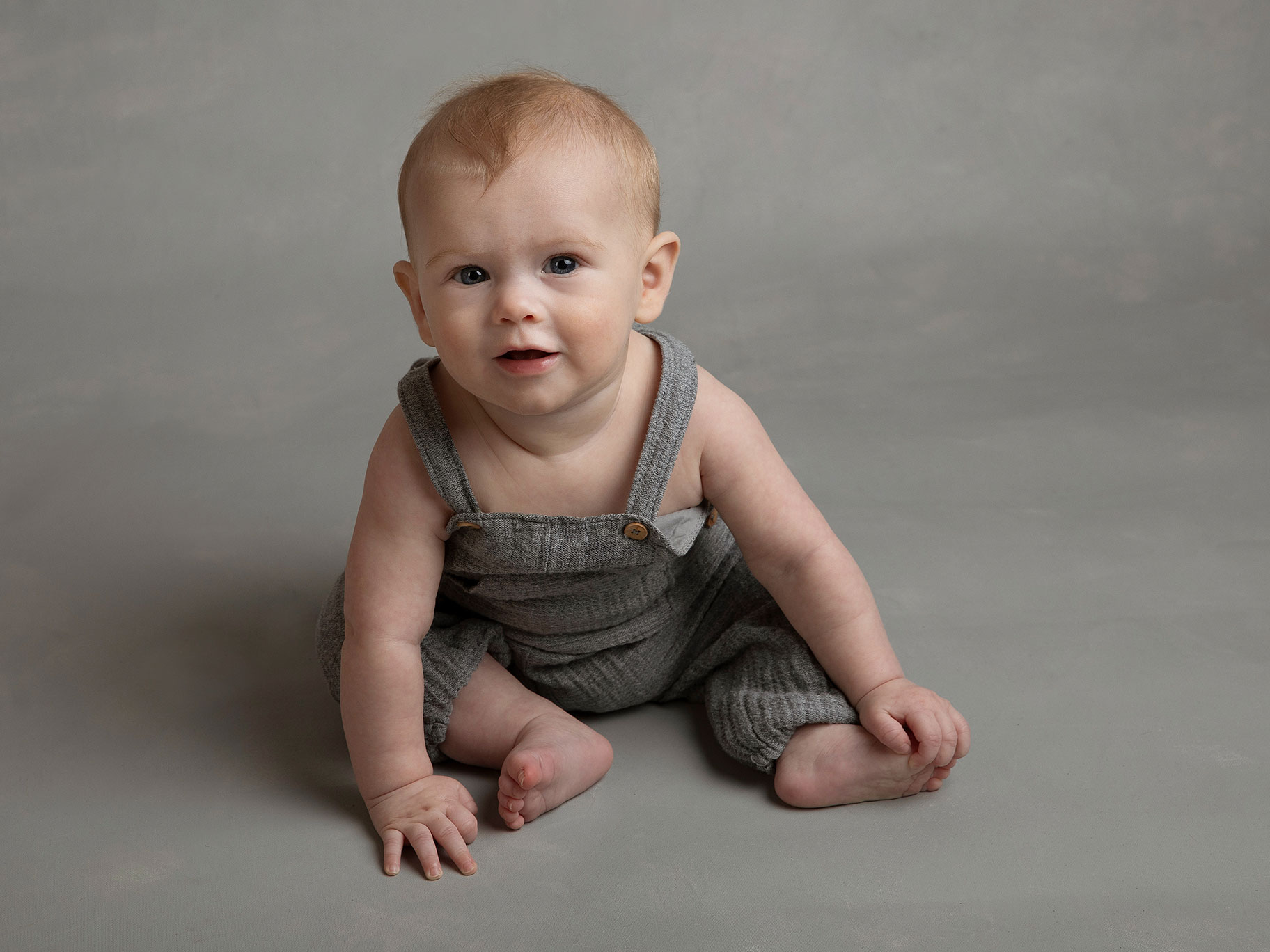 Liten babypojke sitter på golvet och håller om sin ena fot.